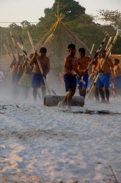 Índio saltando com vara sobre uma tora no chão